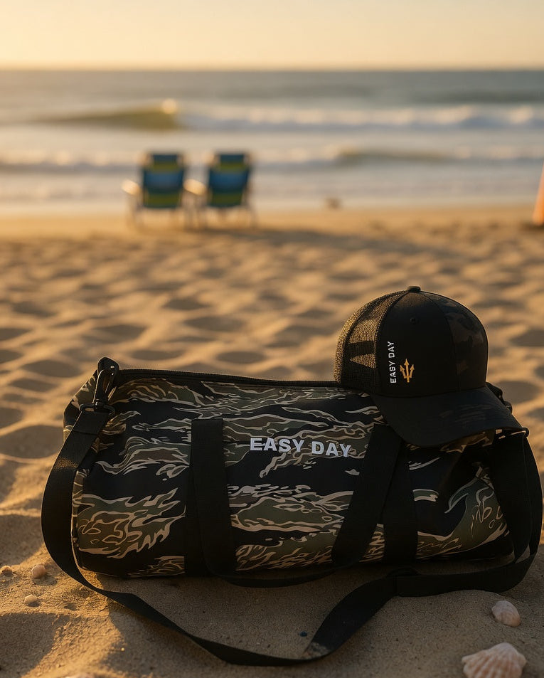Camouflage duffel bag with 'Easy Day' branding on a sandy beach.