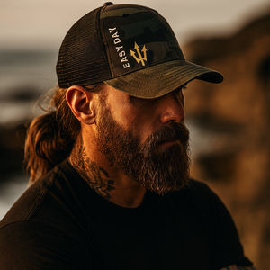 Man wearing a cap with a logo and text, standing against a blurred natural background