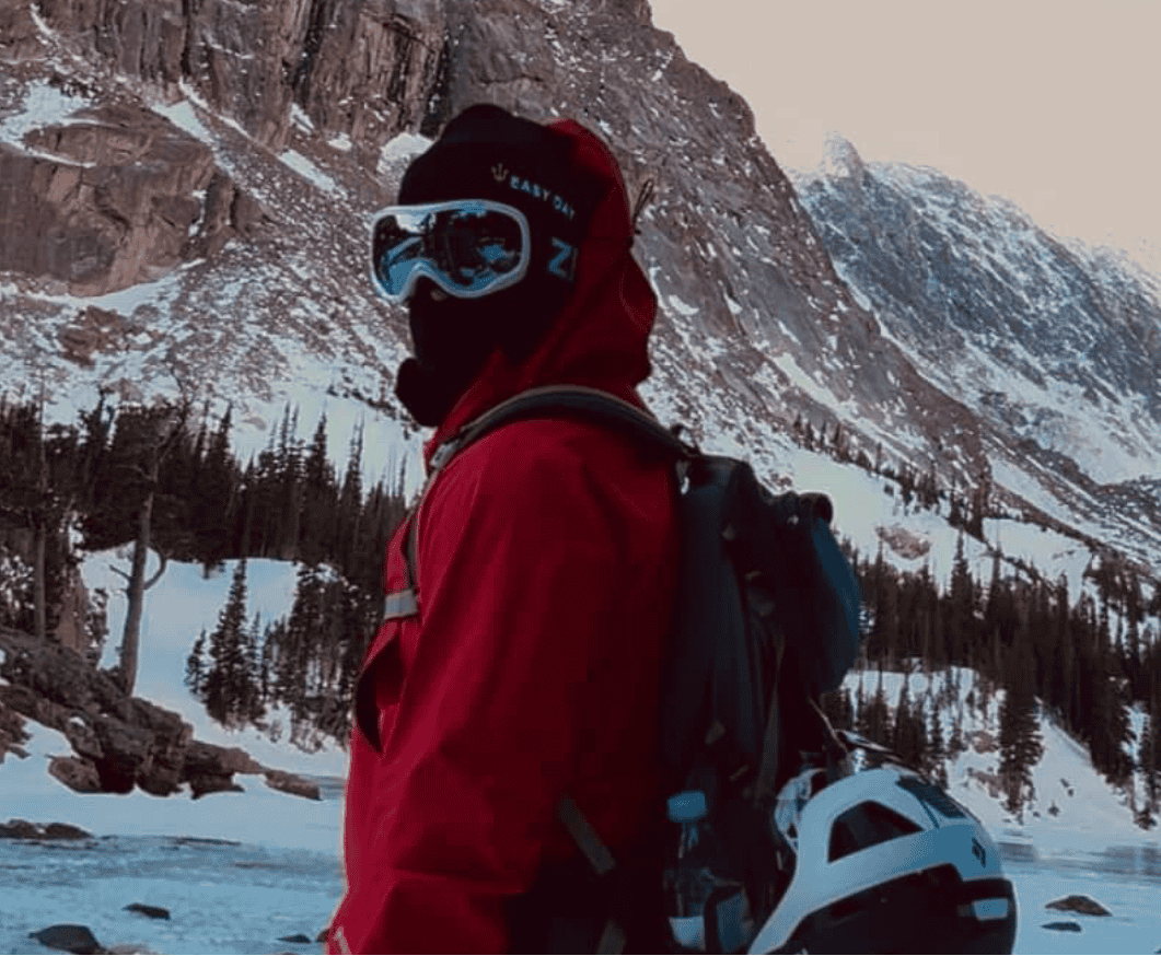 Person in a red jacket with goggles on their head, standing in front of a mountain with 'Easy Day' branding.