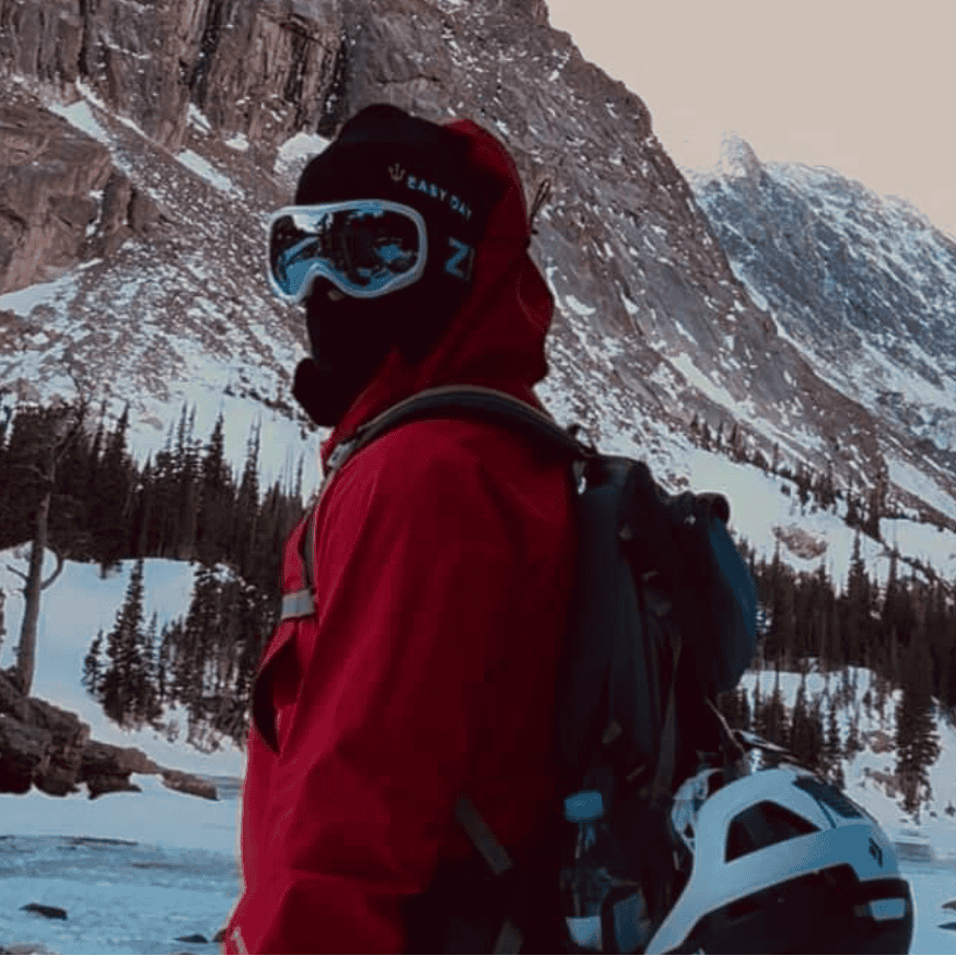 Person in a red jacket with goggles on their head, standing in front of a mountain with 'Easy Day' branding.