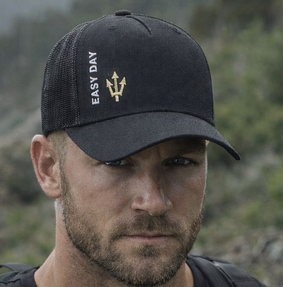 Man wearing a black cap and t-shirt with a backpack, standing outdoors.