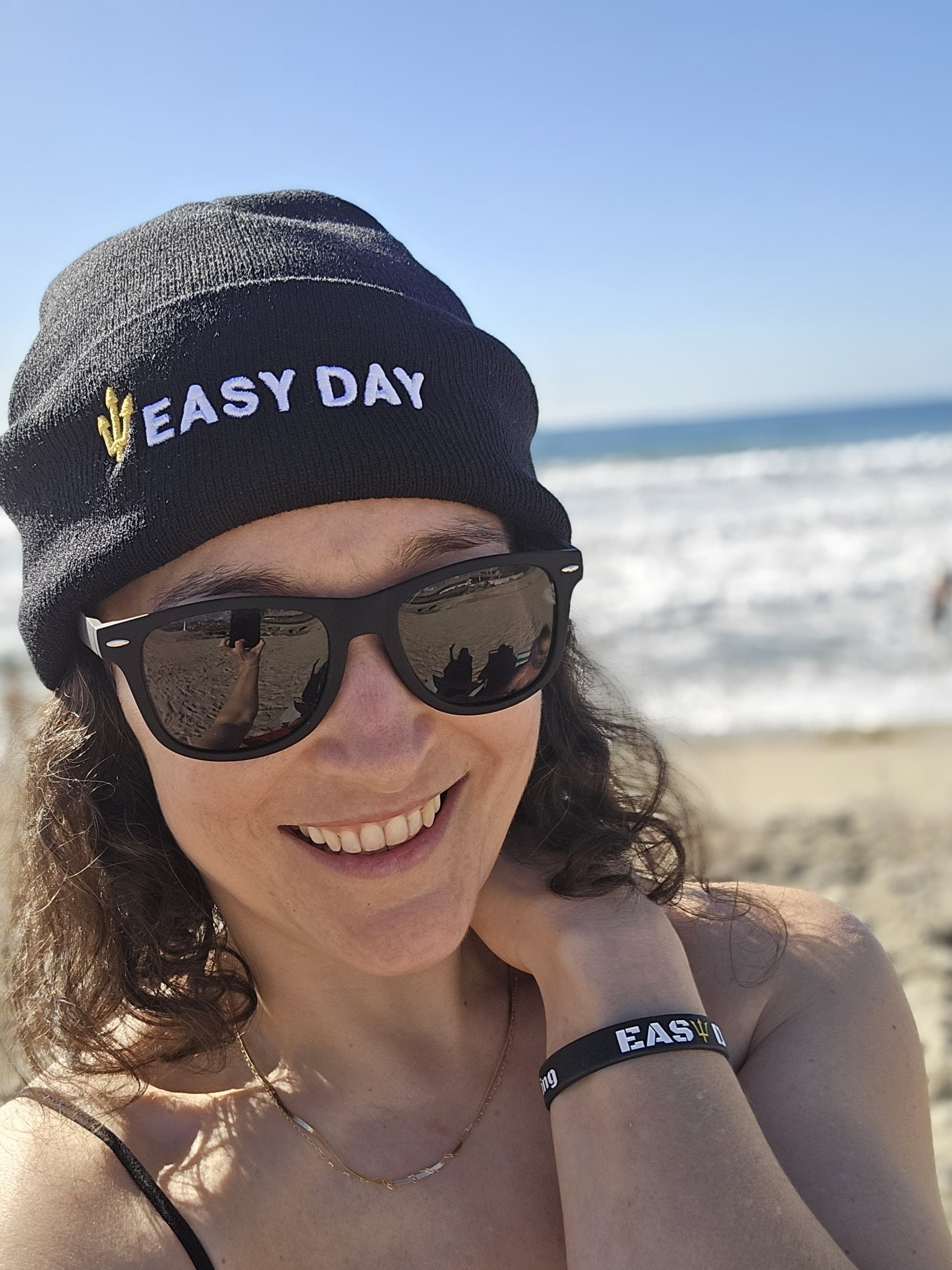 Person wearing an 'Easy Day' beanie and sunglasses on a beach