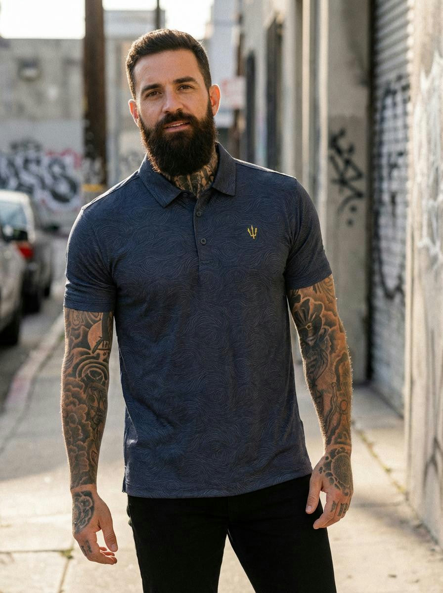 Man with tattoos wearing a blue polo shirt standing on a street with graffiti.
