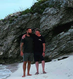 Two men standing on a beach with rocky cliffs in the background