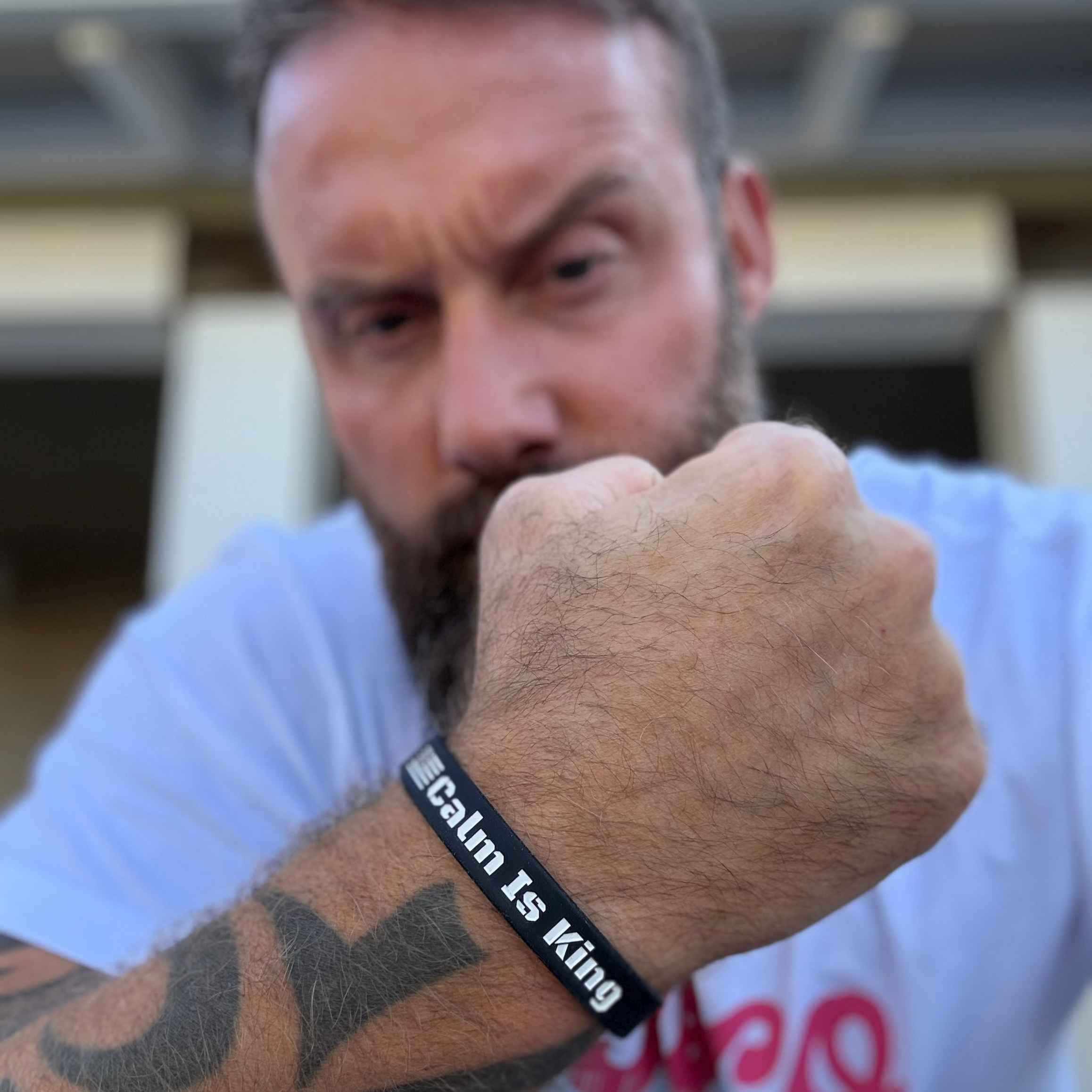 Man with tattooed arm wearing a wristband with 'calm is king' text, blurred background